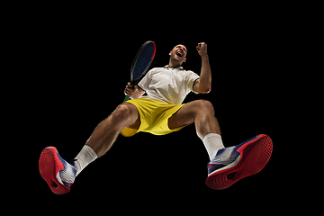 Image showing Young caucasian tennis player in action, motion isolated on black background, look from the bottom. Concept of sport, movement, energy and dynamic.