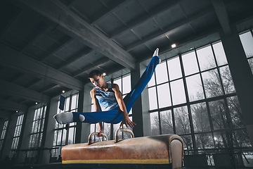 Image showing Little male gymnast training in gym, flexible and active. Caucasian fit little boy, athlete in sportswear practicing in exercises for strength, balance.