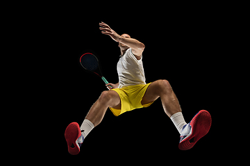 Image showing Young caucasian tennis player in action, motion isolated on black background, look from the bottom. Concept of sport, movement, energy and dynamic.