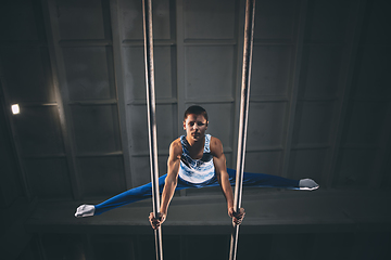 Image showing Little male gymnast training in gym, flexible and active. Caucasian fit little boy, athlete in sportswear practicing in exercises for strength, balance.