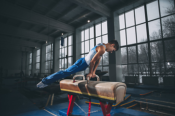 Image showing Little male gymnast training in gym, flexible and active. Caucasian fit little boy, athlete in sportswear practicing in exercises for strength, balance.