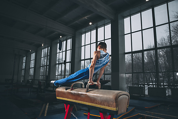 Image showing Little male gymnast training in gym, flexible and active. Caucasian fit little boy, athlete in sportswear practicing in exercises for strength, balance.