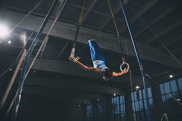 Image showing Little male gymnast training in gym, flexible and active. Caucasian fit little boy, athlete in sportswear practicing in exercises for strength, balance.