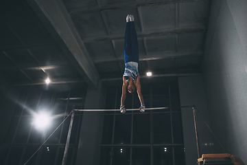 Image showing Little male gymnast training in gym, flexible and active. Caucasian fit little boy, athlete in sportswear practicing in exercises for strength, balance.