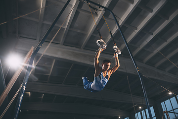 Image showing Little male gymnast training in gym, flexible and active. Caucasian fit little boy, athlete in sportswear practicing in exercises for strength, balance.