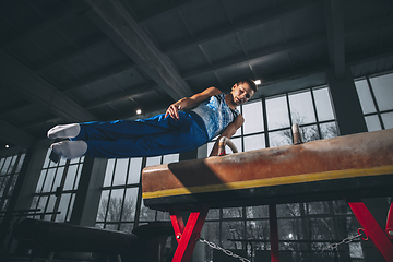 Image showing Little male gymnast training in gym, flexible and active. Caucasian fit little boy, athlete in sportswear practicing in exercises for strength, balance.