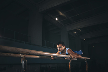 Image showing Little male gymnast training in gym, flexible and active. Caucasian fit little boy, athlete in sportswear practicing in exercises for strength, balance.