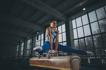 Image showing Little male gymnast training in gym, flexible and active. Caucasian fit little boy, athlete in sportswear practicing in exercises for strength, balance.