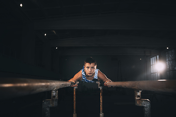 Image showing Little male gymnast training in gym, flexible and active. Caucasian fit little boy, athlete in sportswear practicing in exercises for strength, balance.