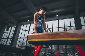 Image showing Little male gymnast training in gym, flexible and active. Caucasian fit little boy, athlete in sportswear practicing in exercises for strength, balance.