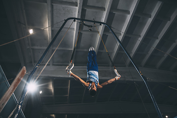 Image showing Little male gymnast training in gym, flexible and active. Caucasian fit little boy, athlete in sportswear practicing in exercises for strength, balance.