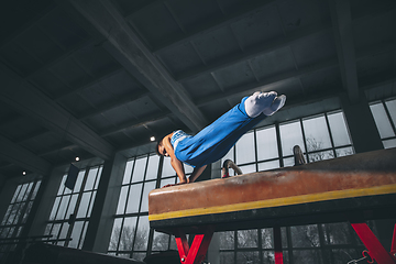 Image showing Little male gymnast training in gym, flexible and active. Caucasian fit little boy, athlete in sportswear practicing in exercises for strength, balance.