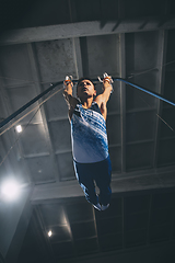 Image showing Little male gymnast training in gym, flexible and active. Caucasian fit little boy, athlete in sportswear practicing in exercises for strength, balance.