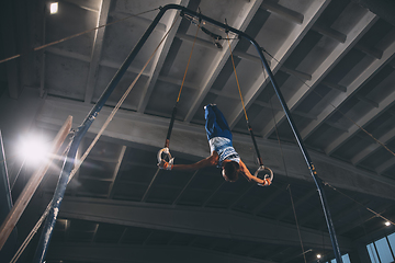 Image showing Little male gymnast training in gym, flexible and active. Caucasian fit little boy, athlete in sportswear practicing in exercises for strength, balance.