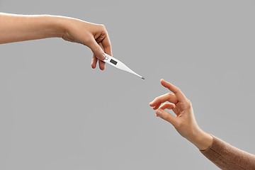 Image showing close up of hands giving each other thermometer