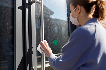 Image showing woman in mask cleaning door handle with wet wipe