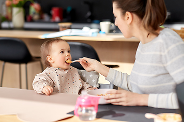 Image showing happy mother feeding baby with puree at home