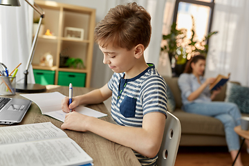 Image showing student boy with book writing to notebook at home