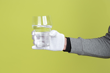 Image showing Male hand wearing white glove holding glass of water isolated on yellow studio background