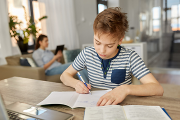 Image showing student boy with book writing to notebook at home