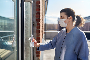 Image showing woman in mask cleaning door handle with wet wipe