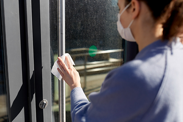 Image showing woman in mask cleaning door handle with wet wipe