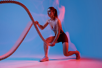 Image showing Caucasian professional female athlete training on blue studio background in neon, mixed light. Muscular, sportive woman.