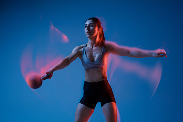 Image showing Caucasian professional female athlete training on blue studio background in neon, mixed light. Muscular, sportive woman.