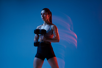 Image showing Caucasian professional female athlete training on blue studio background in neon, mixed light. Muscular, sportive woman.