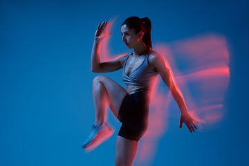Image showing Caucasian professional female athlete training on blue studio background in neon, mixed light. Muscular, sportive woman.