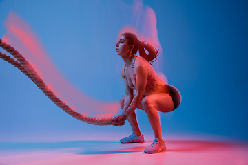 Image showing Caucasian professional female athlete training on blue studio background in neon, mixed light. Muscular, sportive woman.