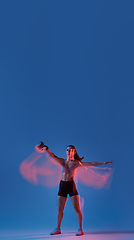 Image showing Caucasian professional female athlete training on blue studio background in neon, mixed light. Muscular, sportive woman.