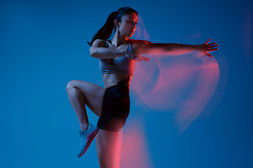 Image showing Caucasian professional female athlete training on blue studio background in neon, mixed light. Muscular, sportive woman.