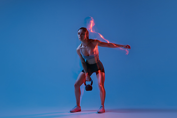 Image showing Caucasian professional female athlete training on blue studio background in neon, mixed light. Muscular, sportive woman.