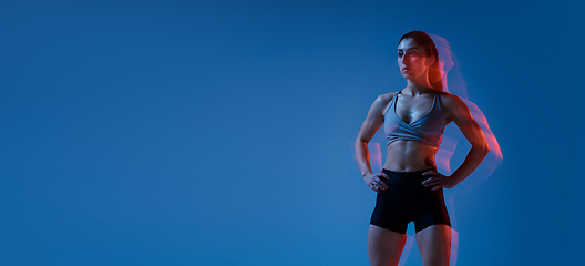 Image showing Caucasian professional female athlete training on blue studio background in neon, mixed light. Muscular, sportive woman.