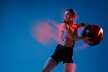 Image showing Caucasian professional female athlete training on blue studio background in neon, mixed light. Muscular, sportive woman.