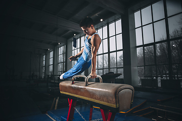 Image showing Little male gymnast training in gym, flexible and active. Caucasian fit little boy, athlete in sportswear practicing in exercises for strength, balance.