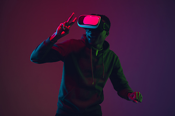Image showing African-american man\'s portrait in VR-headset isolated on gradient studio background in neon light