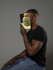 Image showing Be safe and read to become someone else - man covering face with book in face mask while reading on grey background