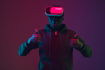 Image showing African-american man\'s portrait in VR-headset isolated on gradient studio background in neon light