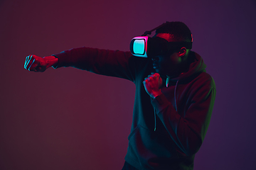 Image showing African-american man\'s portrait in VR-headset isolated on gradient studio background in neon light