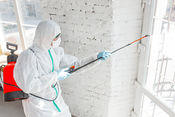 Image showing Coronavirus Pandemic. A disinfector in a protective suit and mask sprays disinfectants in the house or office