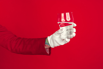 Image showing Female hand in white glove holding glass of pure water on red background