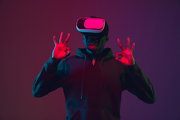 Image showing African-american man\'s portrait in VR-headset isolated on gradient studio background in neon light