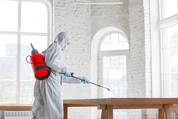 Image showing Coronavirus Pandemic. A disinfector in a protective suit and mask sprays disinfectants in the house or office