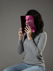 Image showing Be safe and read to become someone else - woman covering face with book in face mask while reading on grey background