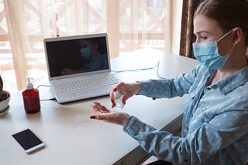 Image showing Young woman in face mask disinfecting gadgets surfaces on her workplace