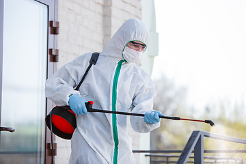 Image showing Coronavirus Pandemic. A disinfector in a protective suit and mask sprays disinfectants in the house or office