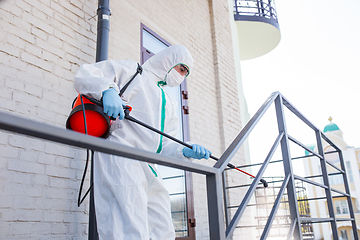 Image showing Coronavirus Pandemic. A disinfector in a protective suit and mask sprays disinfectants in the house or office