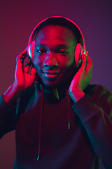 Image showing African-american man\'s portrait with headphones isolated on gradient studio background in neon light